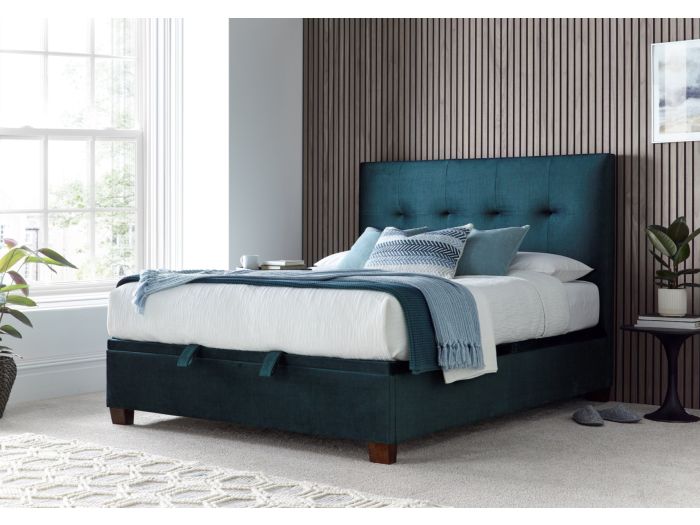 Luxurious deep blue velvet ottoman bed frame with modern dark wooden feet.